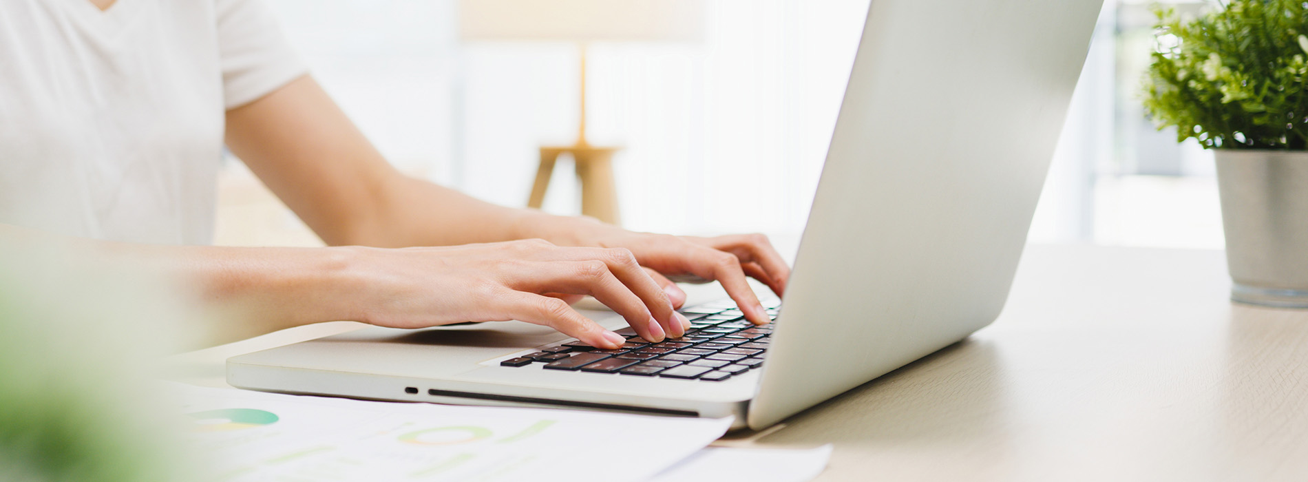 A person typing on a laptop at a desk with a blurred background.