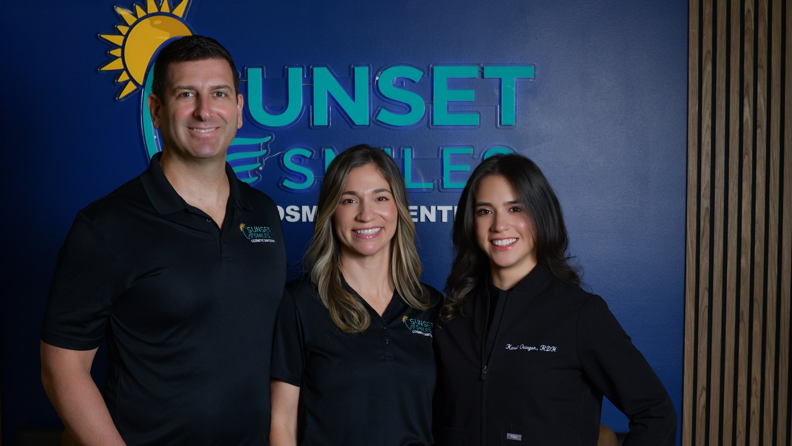The full bilingual Sunset Smiles team at the logo wall in Jupiter, FL