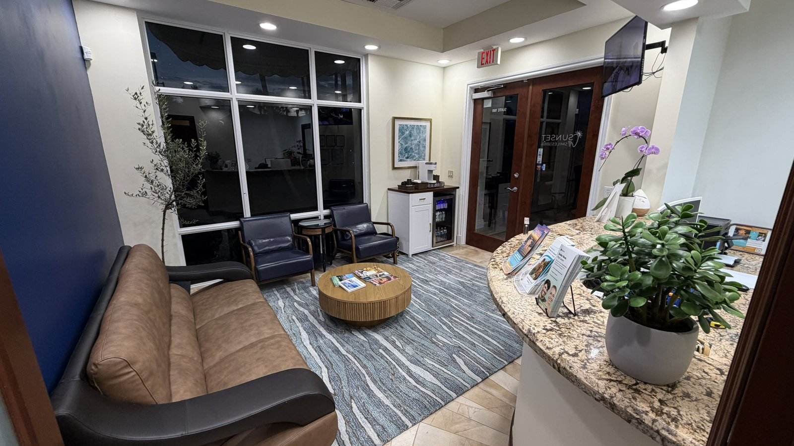 Front desk and reception counter at Sunset Smiles Cosmetic Dentistry, Suite 100, showing the granite counter with orchid and new patient information