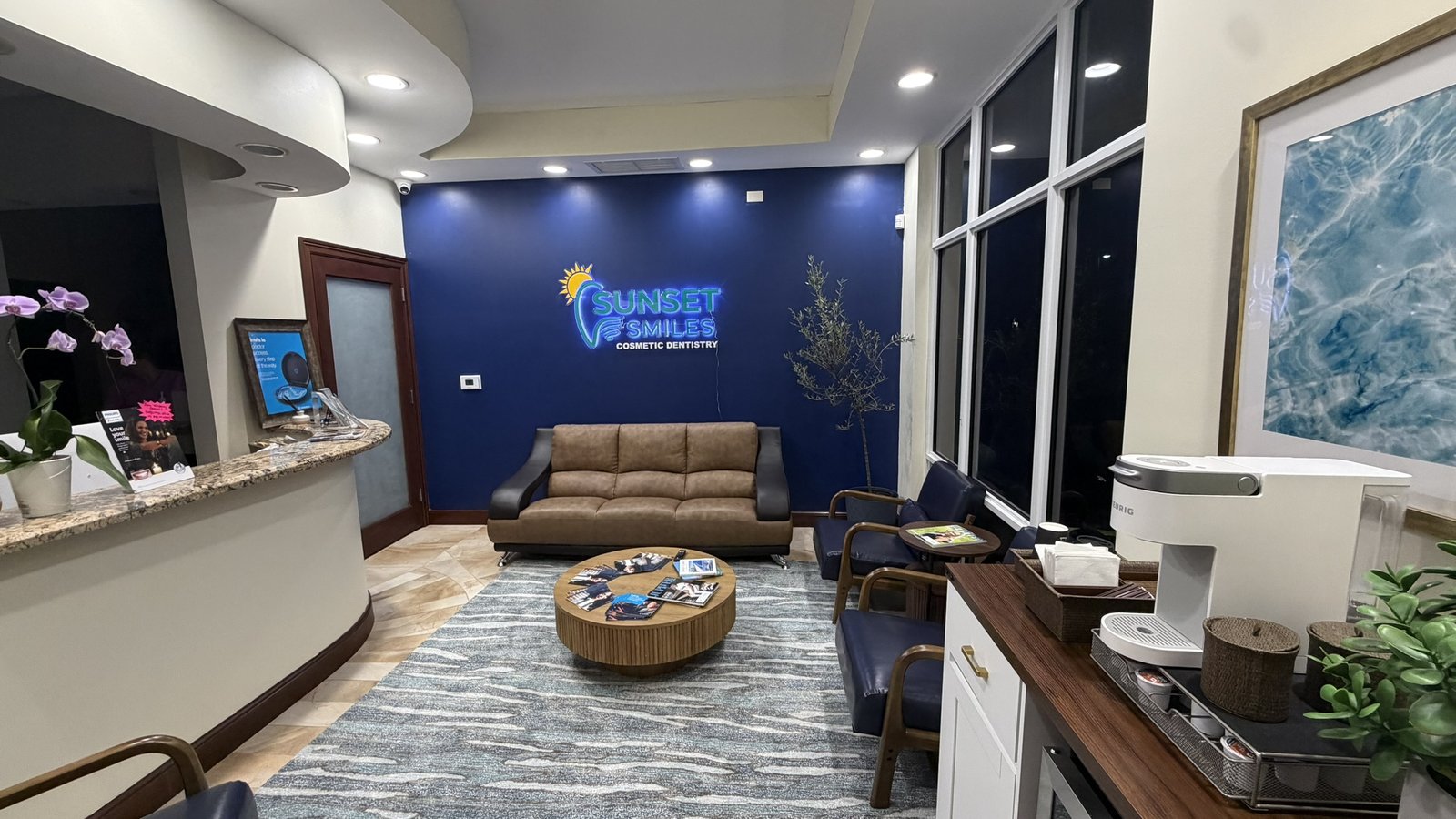 Wide interior view of Sunset Smiles Cosmetic Dentistry office in Jupiter FL — Suite 100 glass entrance with etched brand logo, reception counter and full waiting area in a single frame