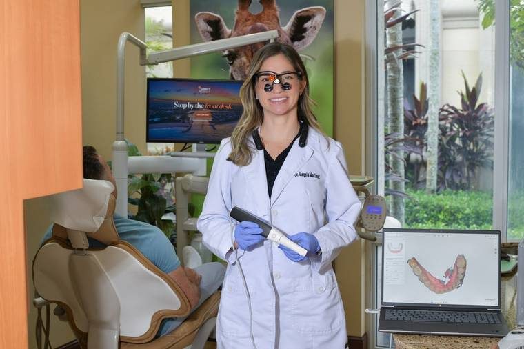 Dr. Magela Martinez holding an intraoral scanner beside a screen showing a 3D scan