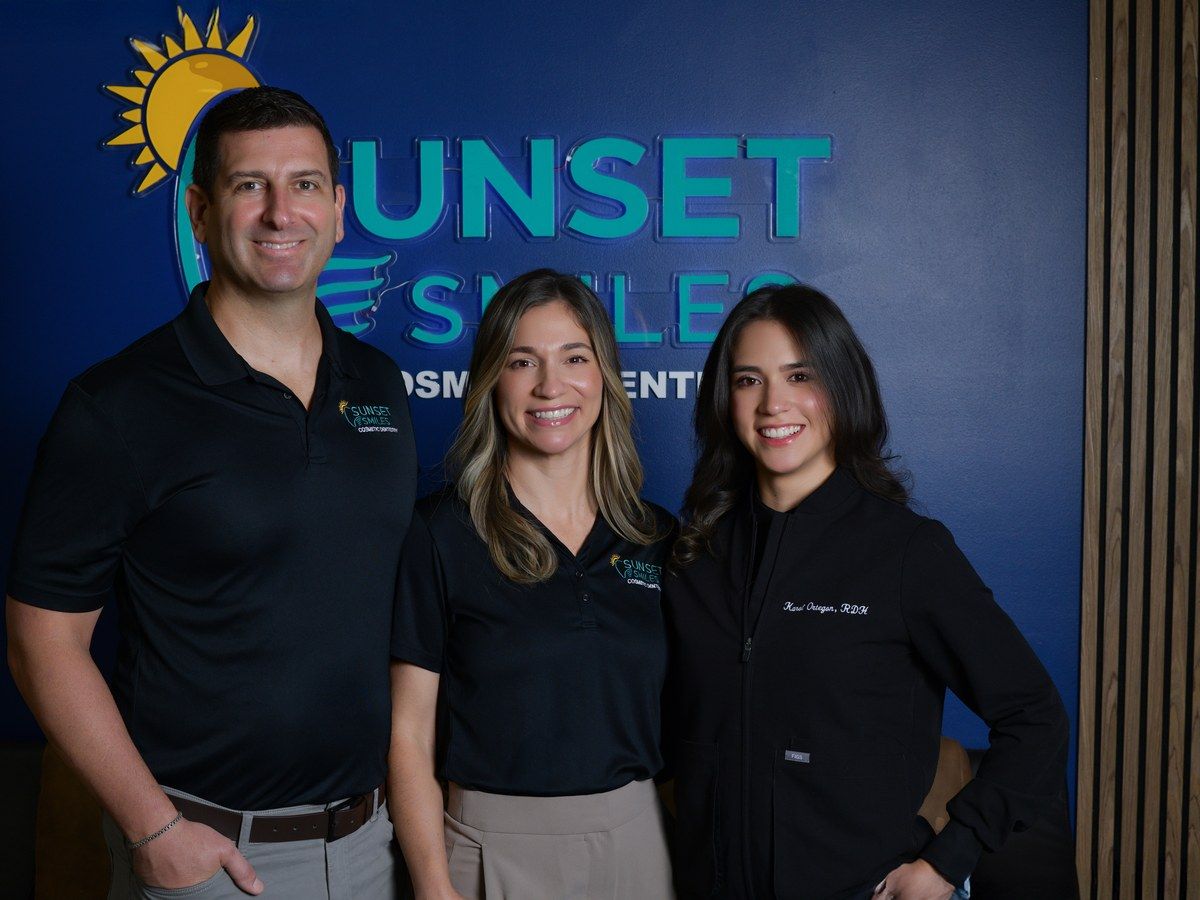 Three members of the Sunset Smiles team in front of the logo in the waiting area at our Jupiter, FL office