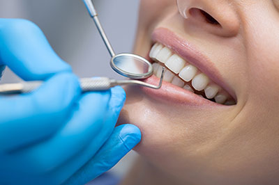 An image of a dental professional performing teeth cleaning on a patient s mouth using a dental drill with a smiling expression.