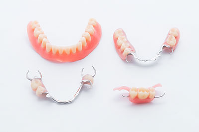 The image displays a set of dentures with red gums and teeth, presented on a white surface against a light background.
