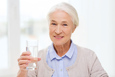The image shows a woman holding a glass of water, smiling gently at the camera.