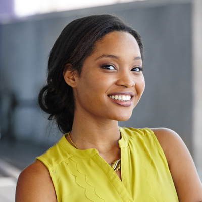 A smiling woman with braided hair wearing a yellow top and posing for a portrait.