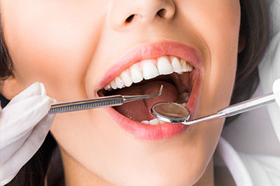 A woman with open mouth under dental instruments, likely during a dental procedure.
