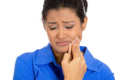 The image shows a woman with her eyes closed, holding her hand near her mouth as if she s rubbing or massaging her face, wearing a blue shirt.